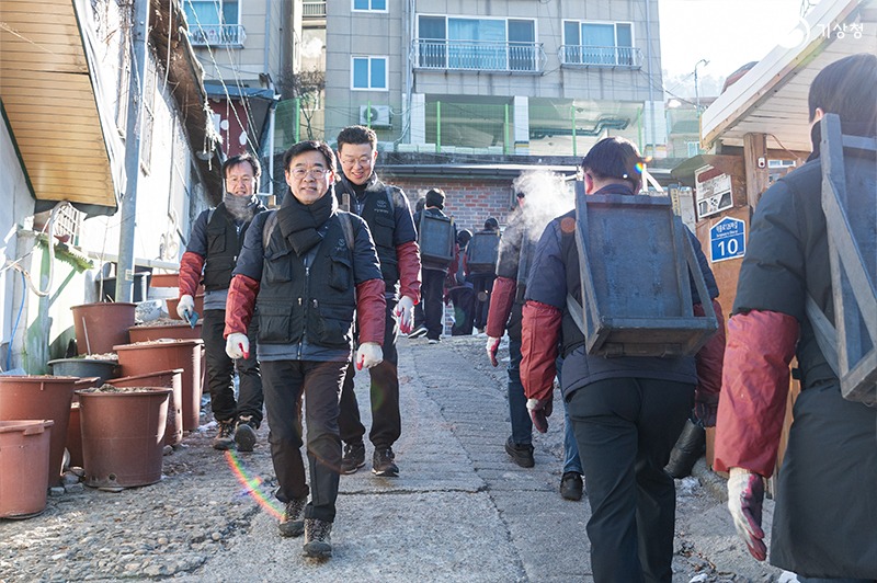 장동언 기상청장과 기상청 직원들이 연탄 배달을 위해 지게를 지고 오르막길을 오르내리는 모습